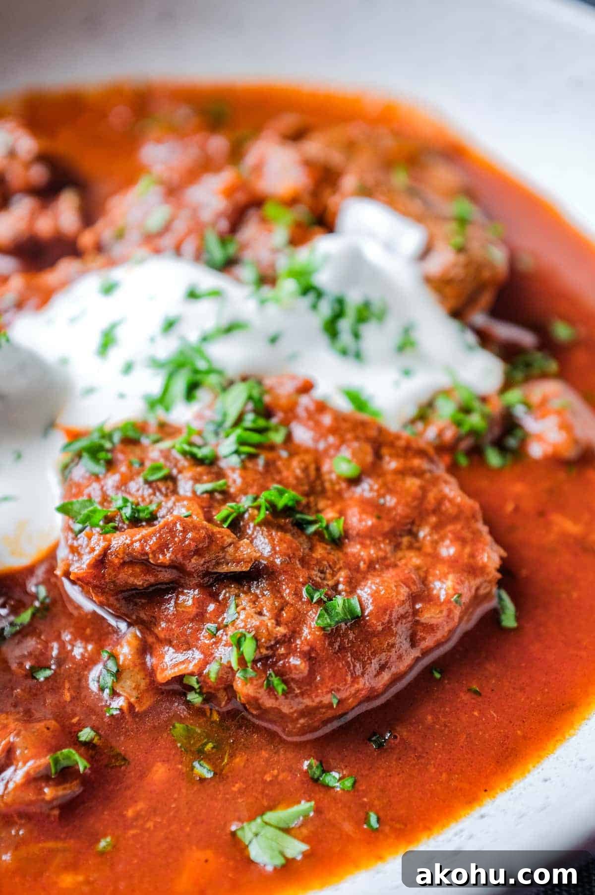 A plate of Hungarian Pörkölt Beef Stew drizzled with sour cream and garnished with parsley