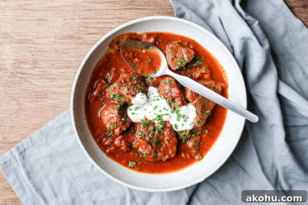 A bowl of Hungarian Pörkölt Beef Stew in a bowl, wrapped in a tea towel.
