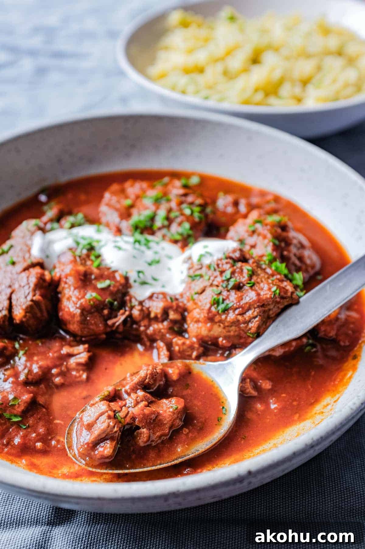 A bowl of Hungarian Pörkölt Beef Stew drizzled with sour cream and garnished with parsley