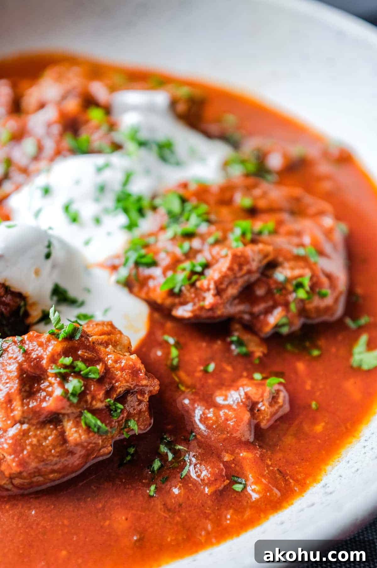 A plate of Hungarian Pörkölt Beef Stew drizzled with sour cream and garnished with parsley