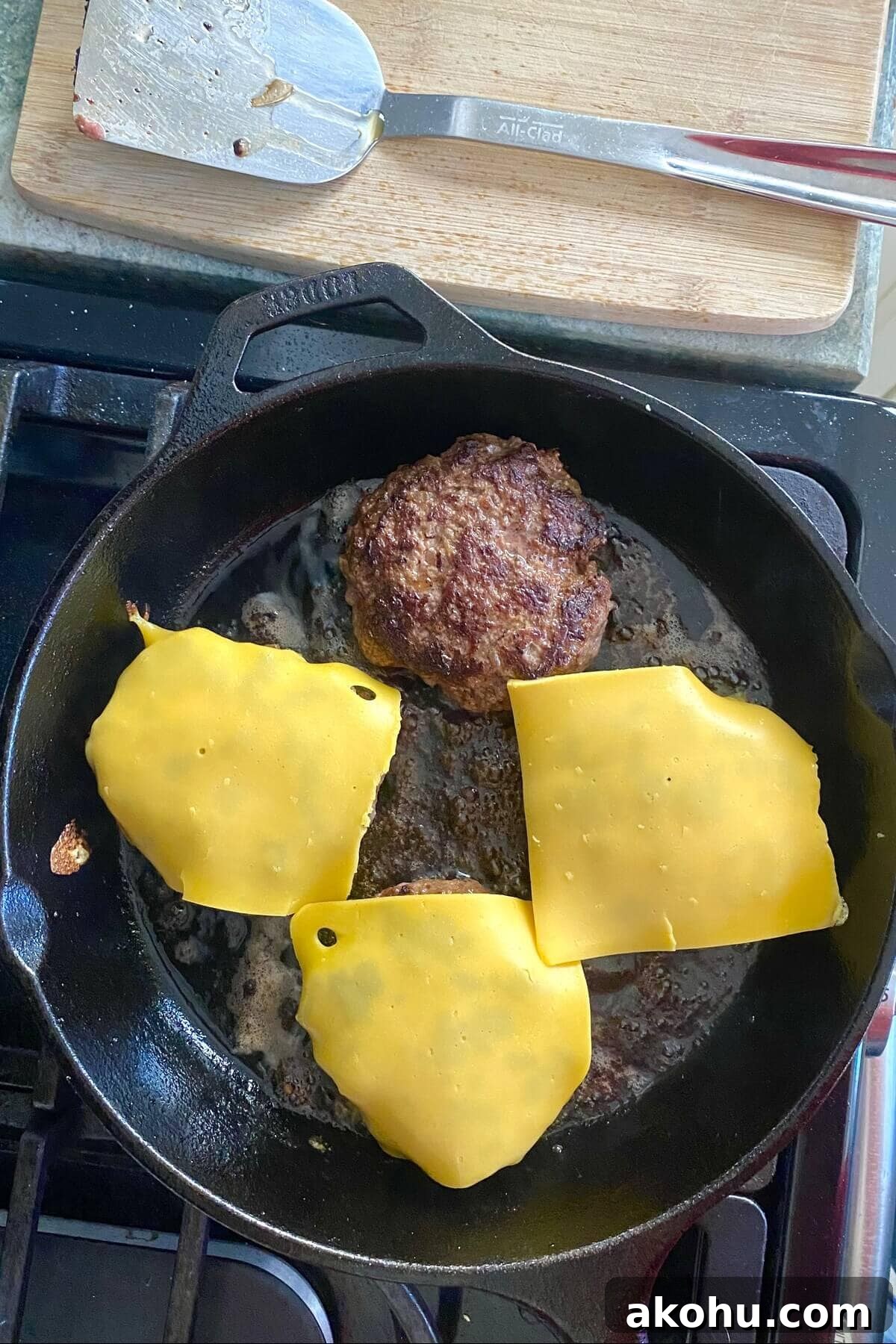 Four hamburgers cooking in a cast iron skillet.
