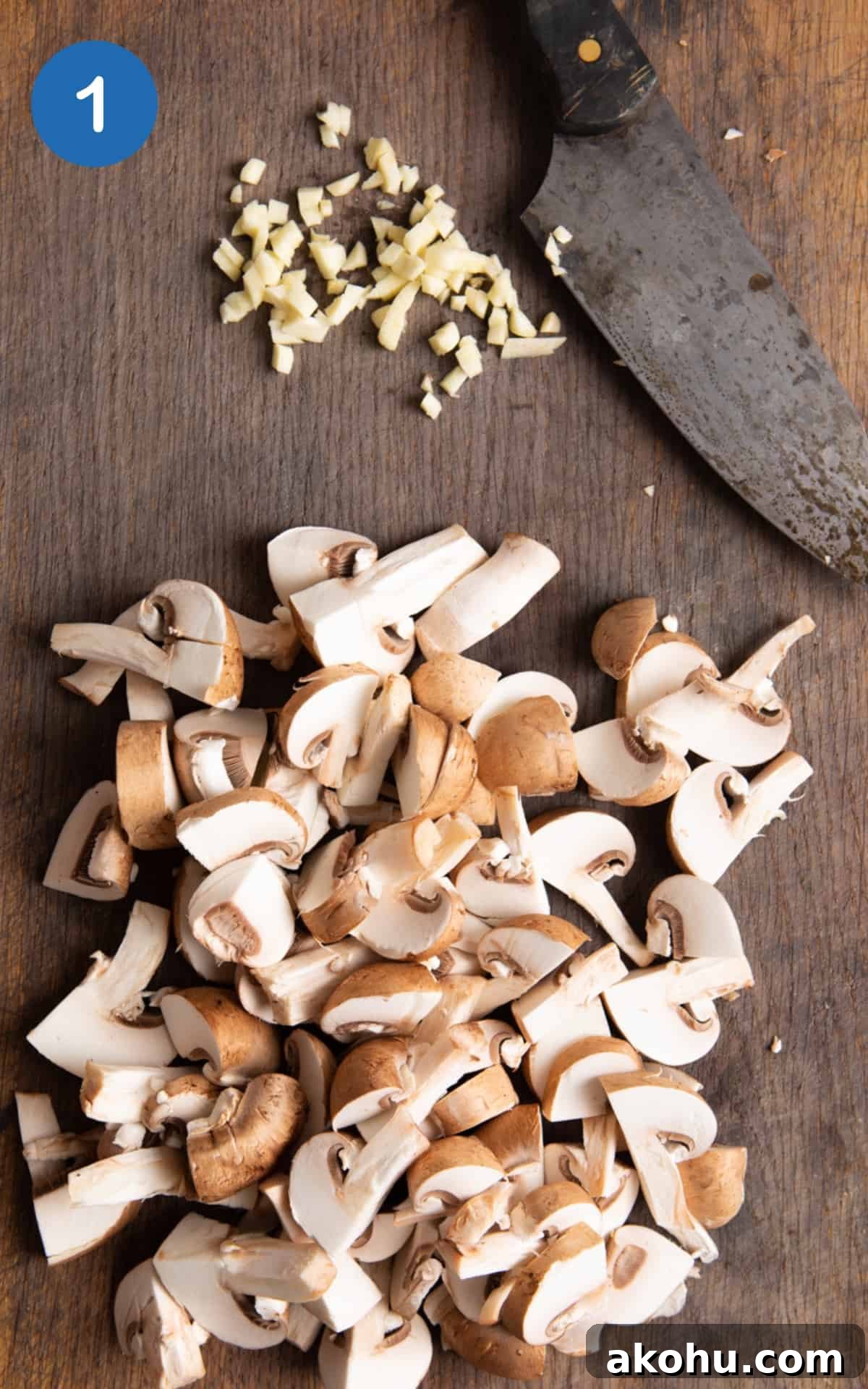 chopped mushrooms and garlic on dark wooden chopping board with sharp knife.