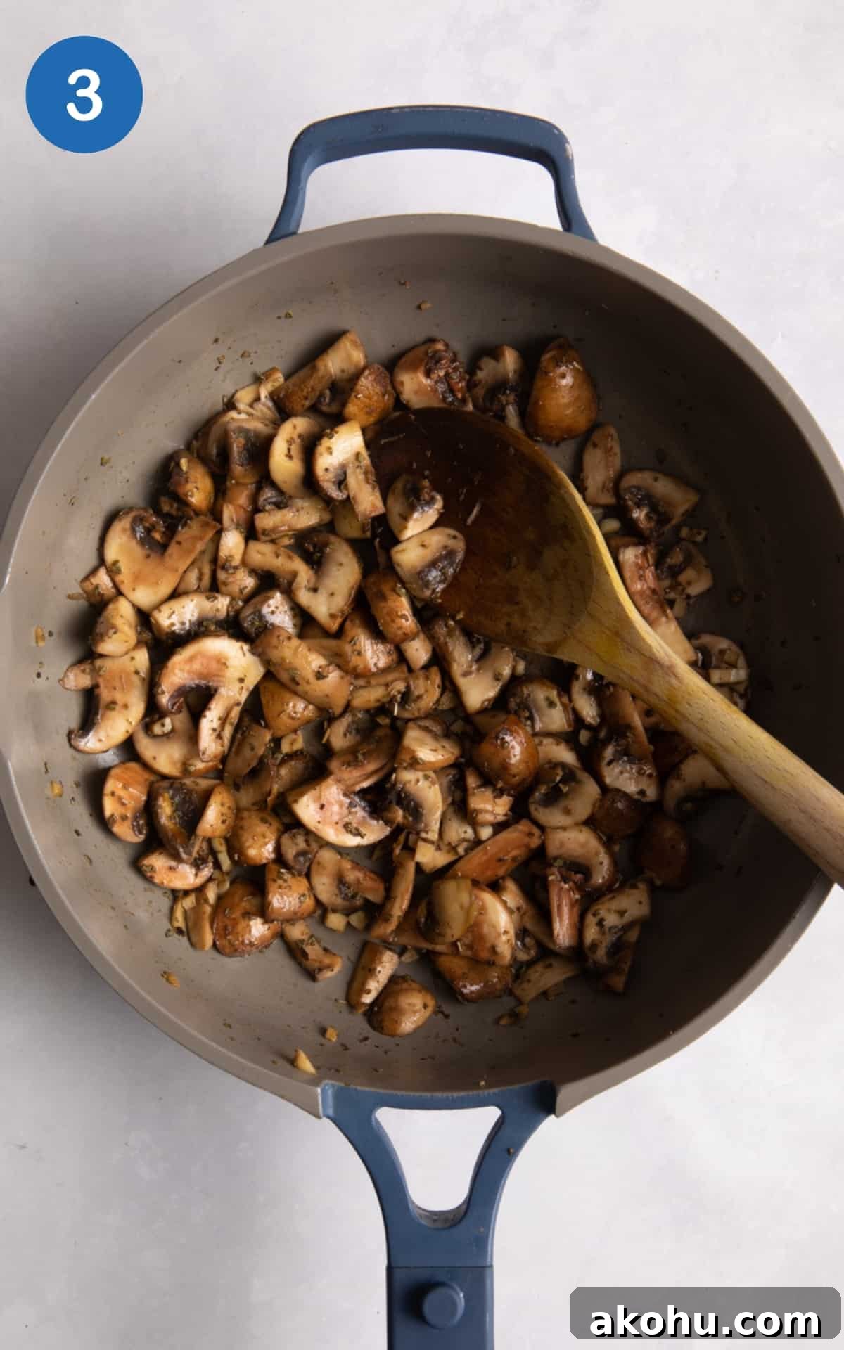 cooked garlic mushrooms in blue frying pan with wooden spoon on white surface.