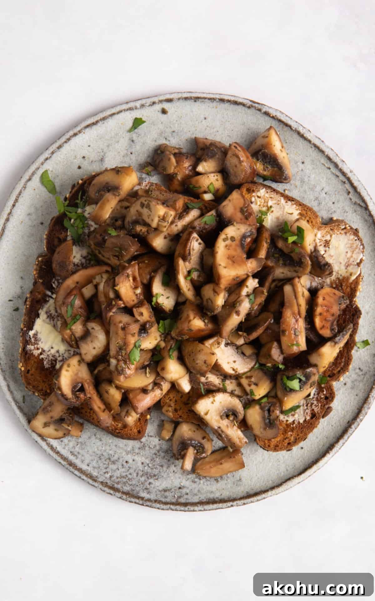 overhead shot of garlic mushrooms on toast on grey plate. Plate Is on white surface.
