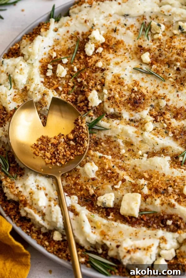Close up view of a bowl of Blue Cheese Mashed Potatoes with Toasted Breadcrumbs with a gold spoon contains more breadcrumbs on top.