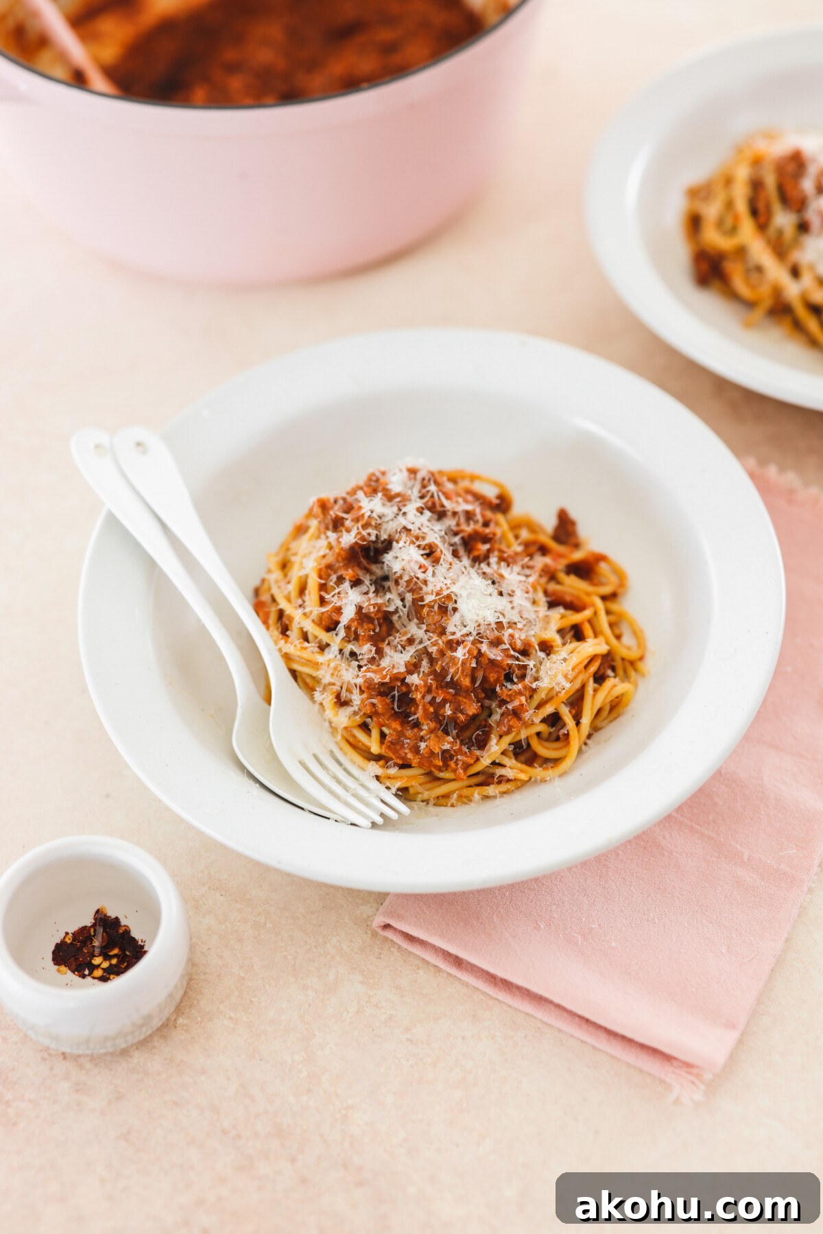 vegan bolognese atop pasta in a white bowl with utensils