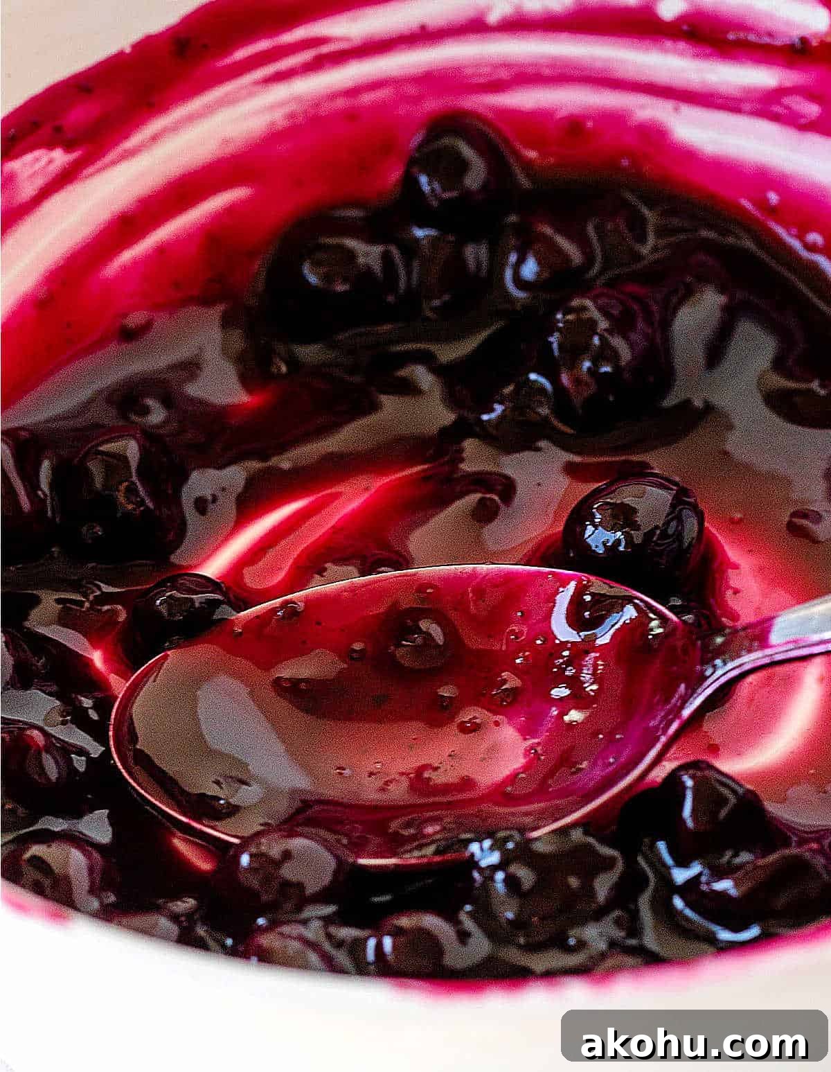 Blueberry Sauce Recipe for Pancakes, Yogurt & Desserts 3 White bowl with blueberry sauce, a spoon. Very close up image.