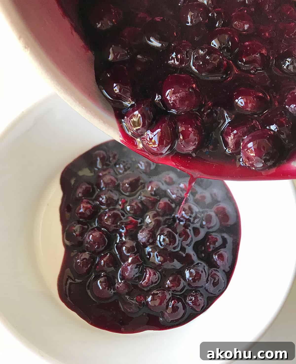Transferring blueberry sauce from saucepan to white bowl.