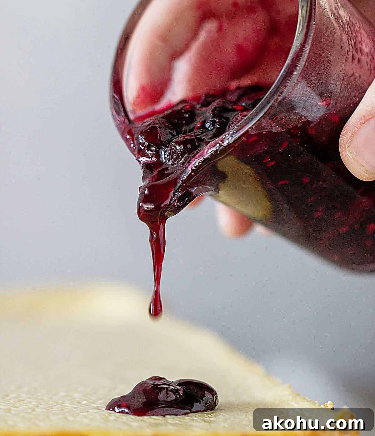 Blueberry Sauce Recipe for Pancakes, Yogurt & Desserts 7 Hand pouring berry sauce from glass jar onto a cheesecake.