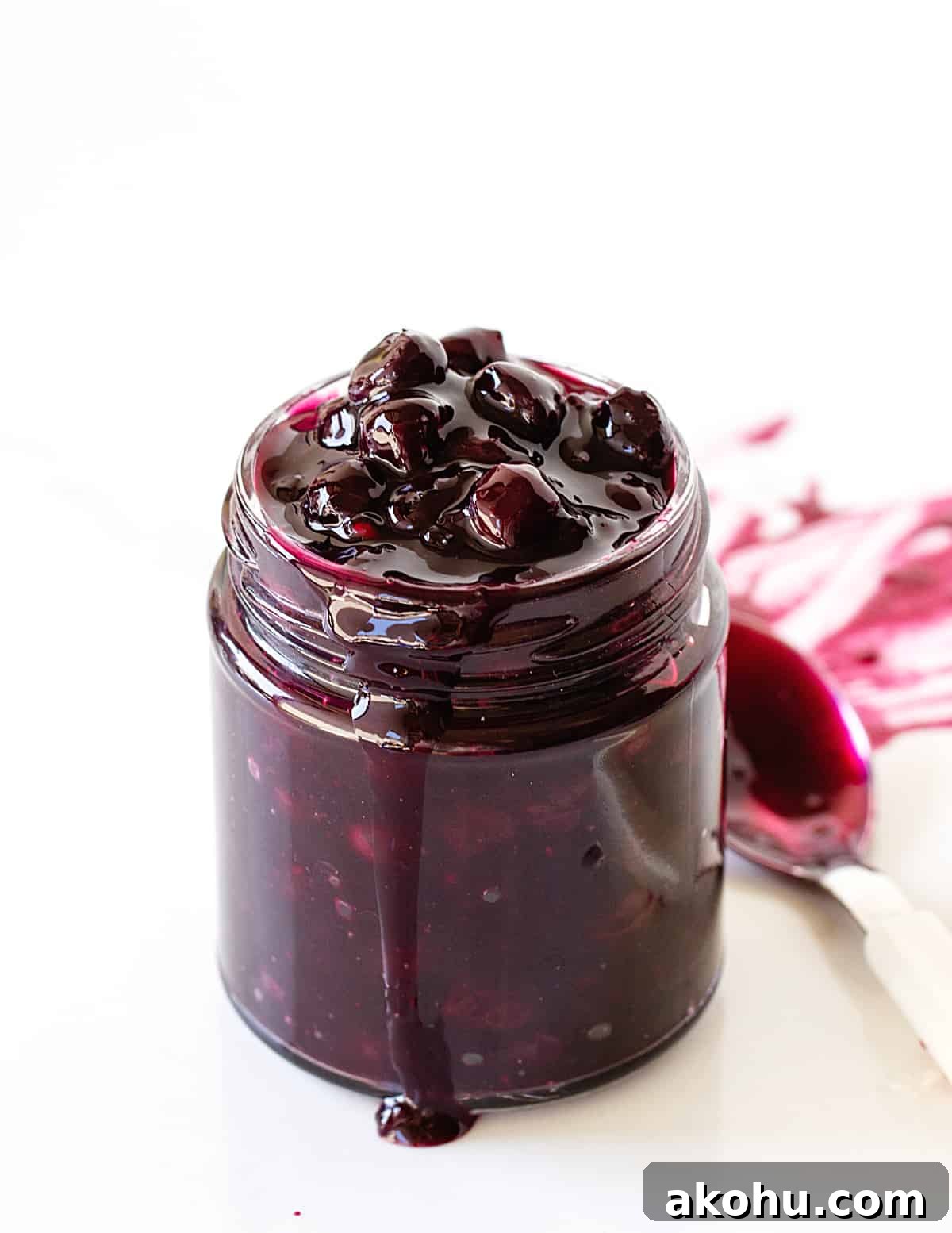 Blueberry Sauce Recipe for Pancakes, Yogurt & Desserts 8 Glass jar with blueberry sauce, drip and spoon, white background