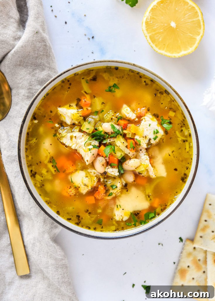 white bean lemon chicken soup in a bowl with veggies and broth, crackers and lemon on the side.