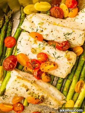 A large pan filled with asparagus, cherry tomatoes and white fish.