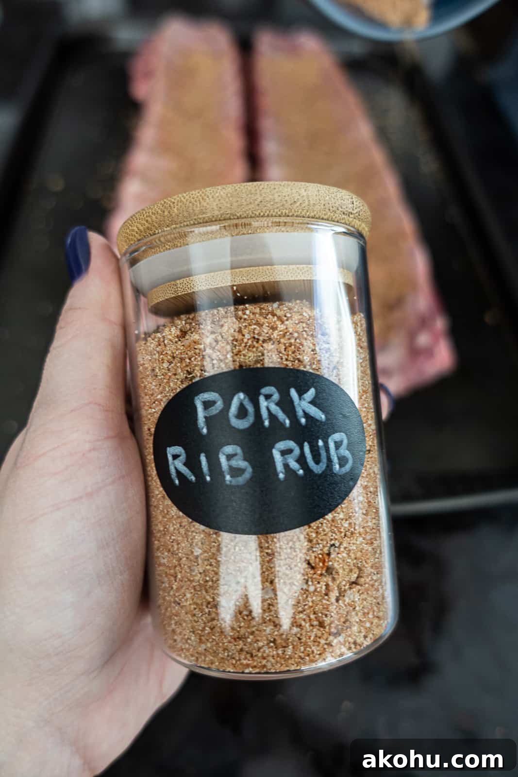 Hand holding pork rib rub infront of ribs