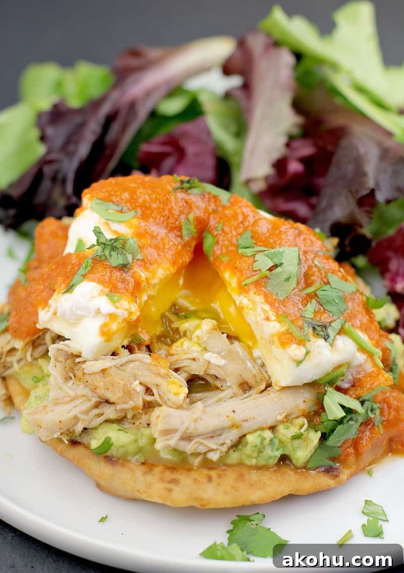 assembled mexican eggs benedict on a white plate with side salad; poached egg on top is split to show runny yolk