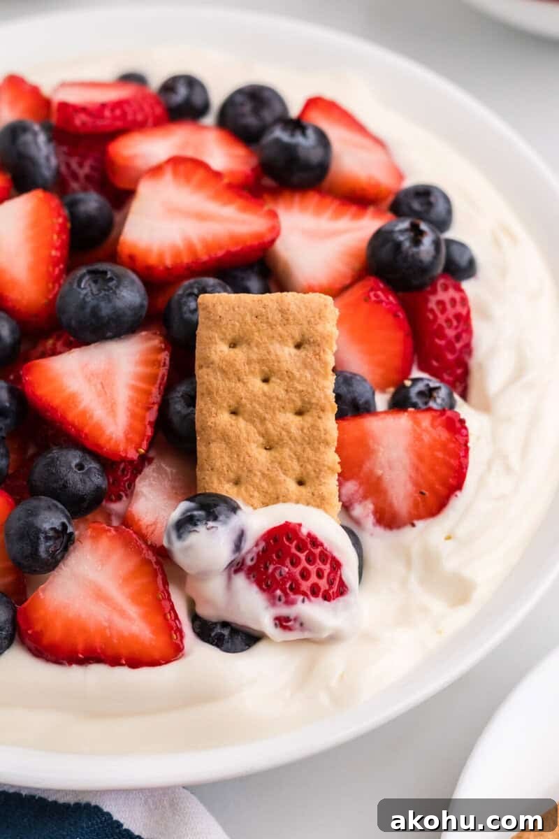 Patriotic Layered Cheesecake Dip for Fourth of July Parties 9 using a graham cracker to eat the dip.