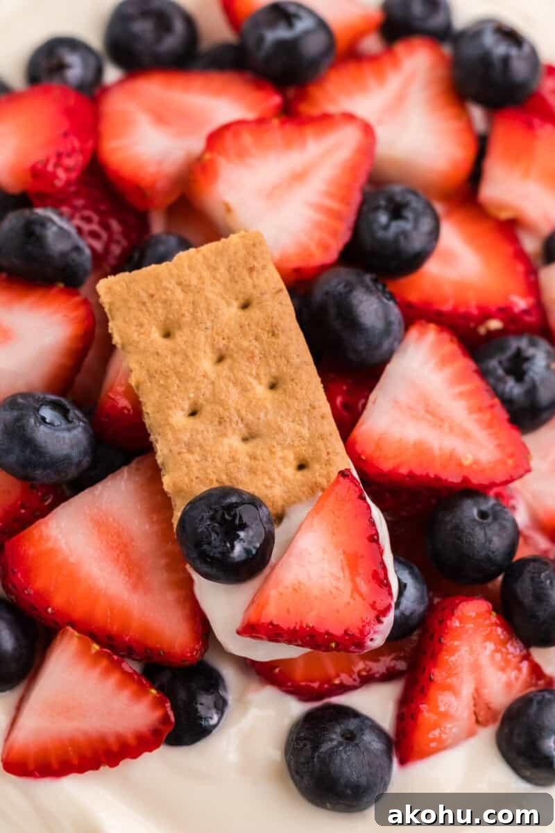 Patriotic Layered Cheesecake Dip for Fourth of July Parties 10 closeup of using a graham cracker to eat the dip.