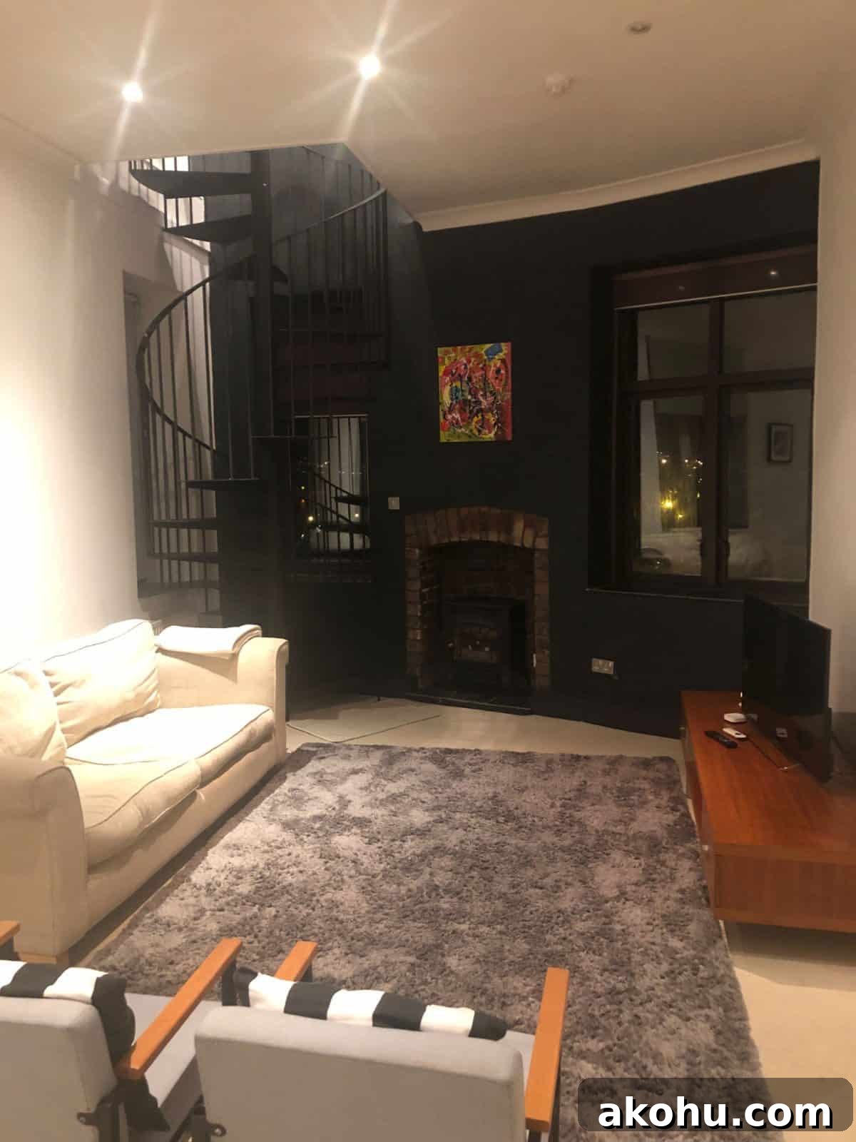 a black metal staircase in the corner of a living room with  a cream sofa and a grey rug and the window at one end