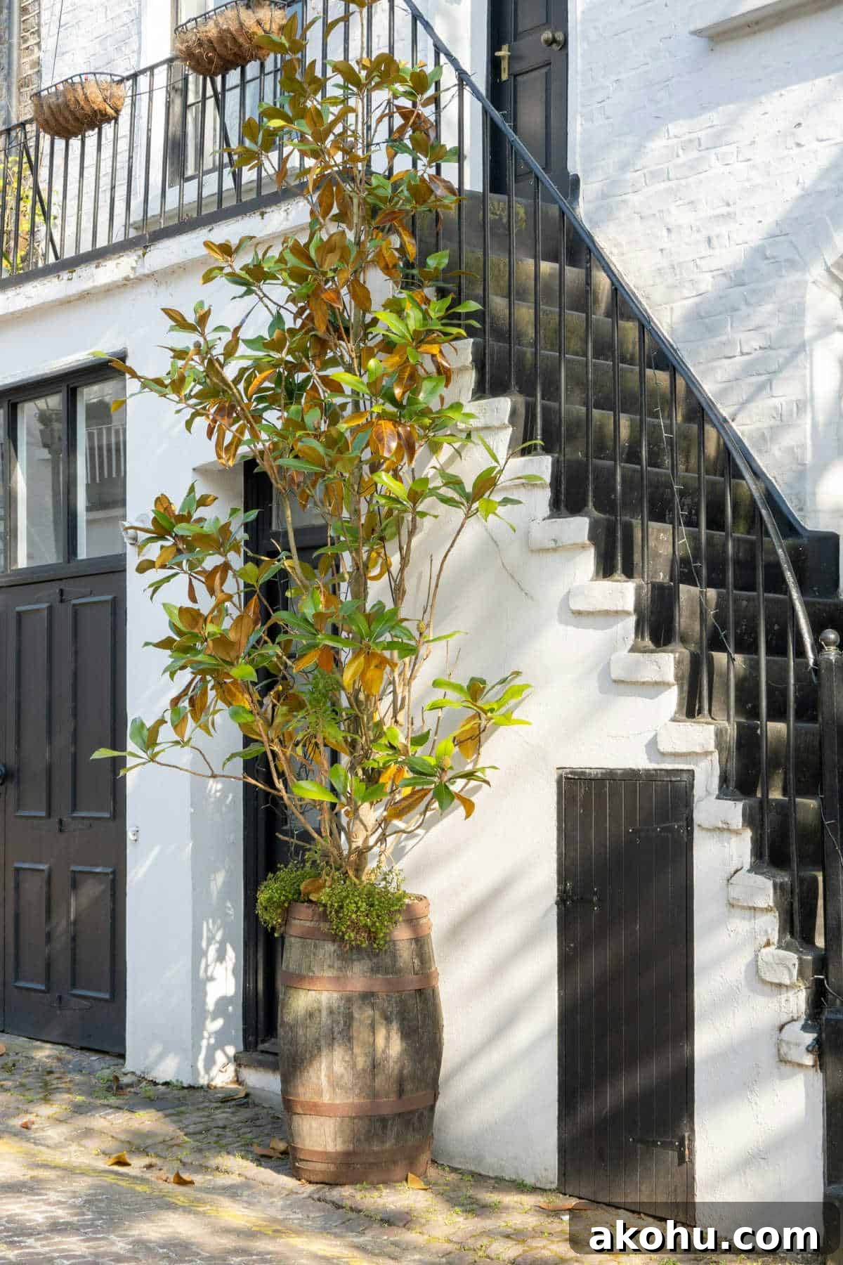 metal staircase leading up to a black door outside a white house with foliage at the side of the stairs