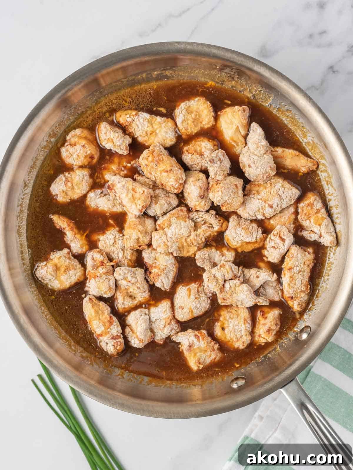 Tossing crispy chicken with the easy orange chicken sauce in a skillet.
