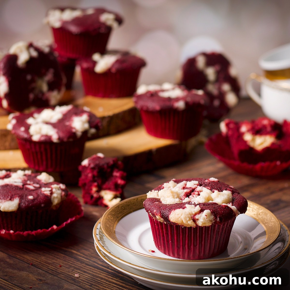 Red Velvet Muffins Filled with Cream Cheese Swirl 3 A cluster of red velvet muffins, some on a wooden tray, some on the table top, and one on a small white plate.