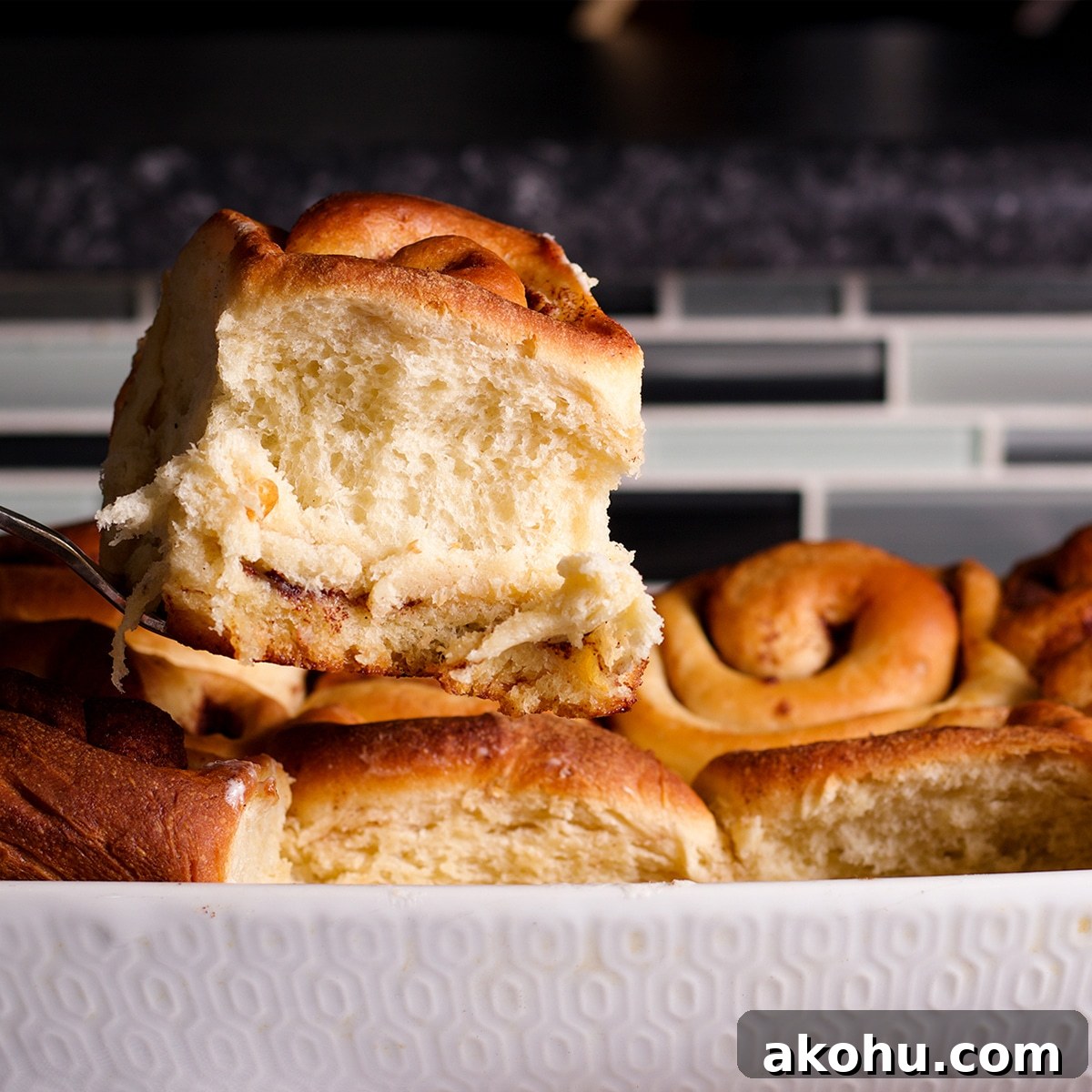 Lifting a freshly baked cinnamon roll from the pan with a spatula.