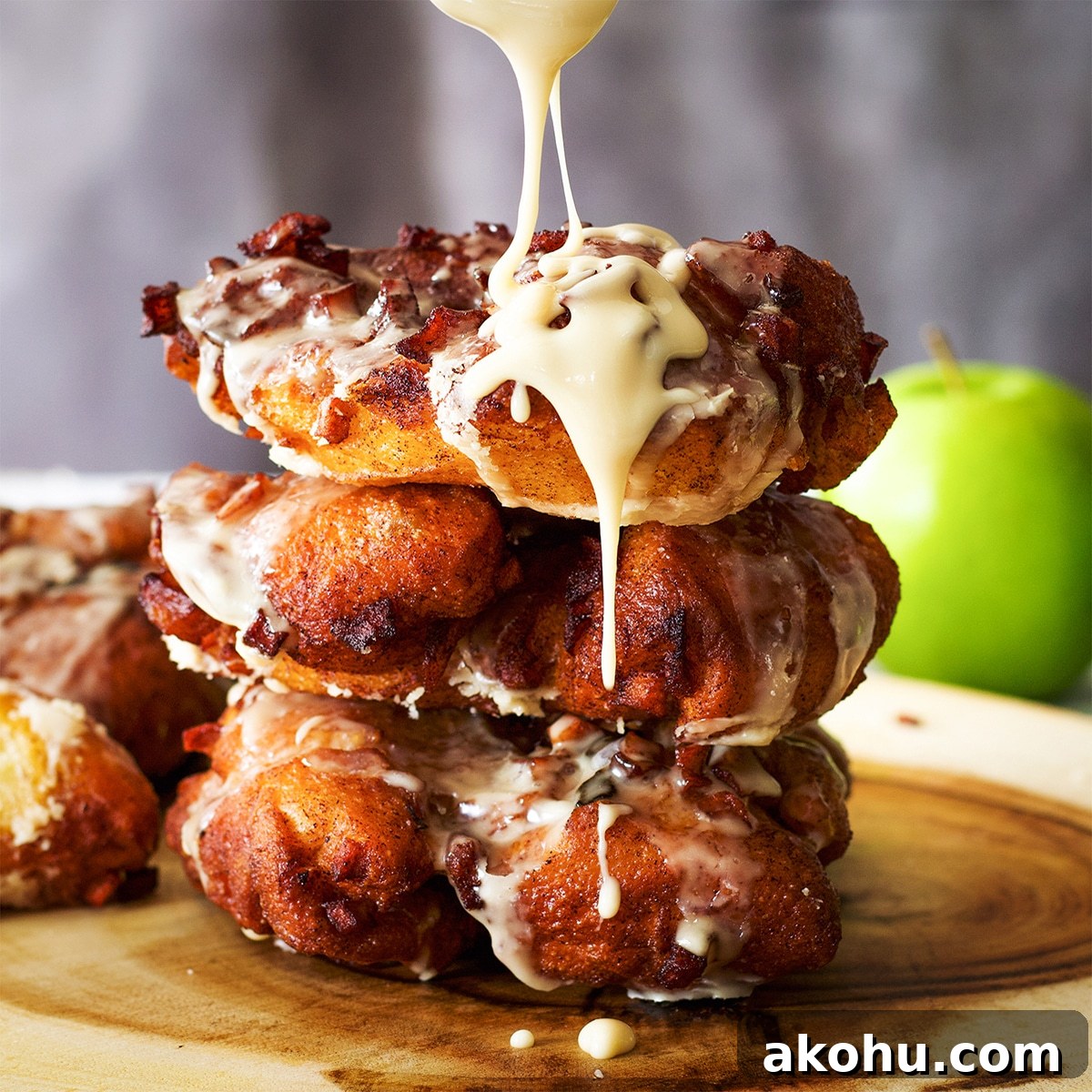 A stack of three homemade apple fritters with maple glaze dripping off the sides.