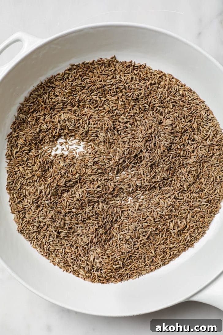 Toasting cumin seeds in a white skillet.