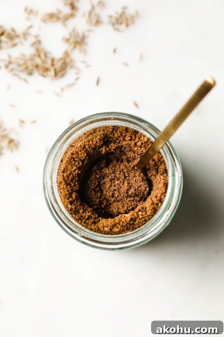 Top view of a jar of cumin powder with a golden spoon inside.