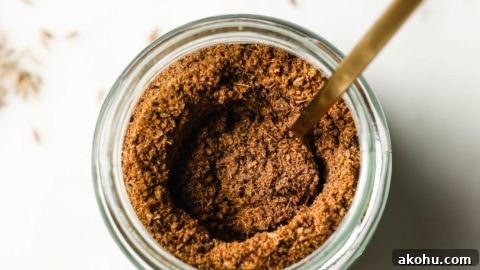 Top view of a jar of cumin powder with a golden spoon inside.