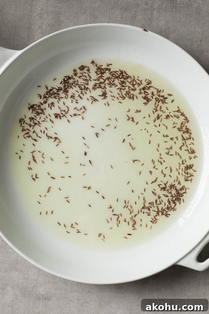Cumin seeds being toasted in hot oil in a white skillet.