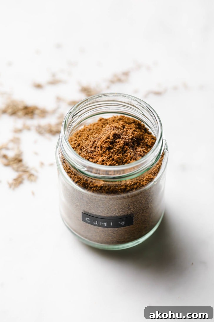 Cumin Powder in a spice jar with coriander seeds scattered around.