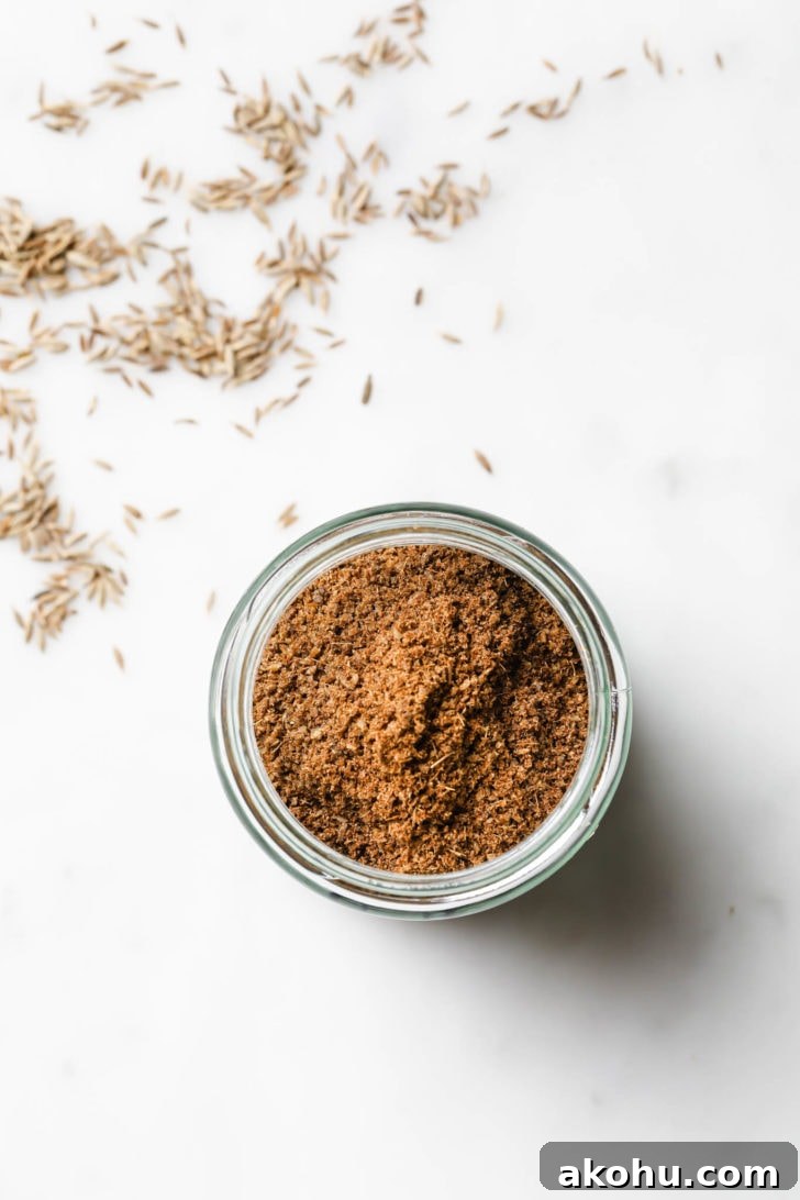 Top view of cumin Powder in a spice jar with coriander seeds scattered around.