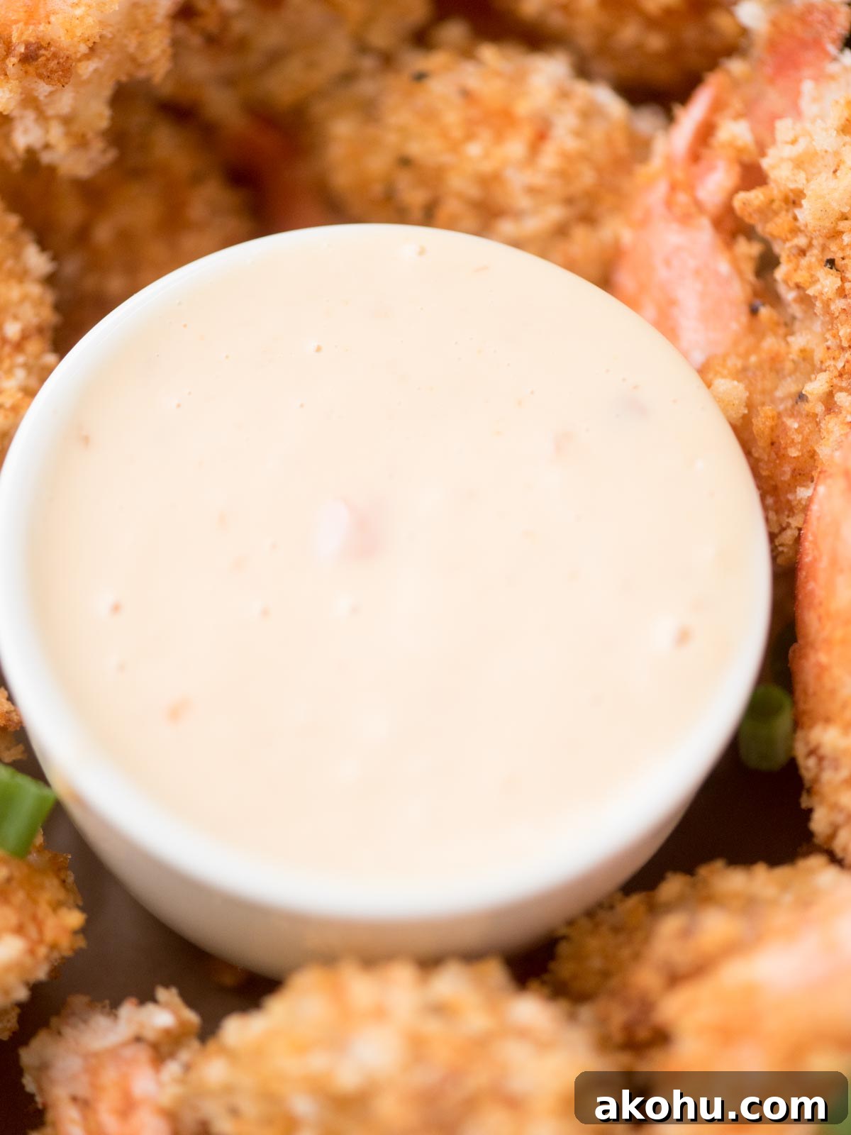 Close-up of a creamy dipping sauce in a white bowl surrounded by breaded fried shrimp. The sauce is pale and smooth, while the shrimp are golden brown and crispy, suggesting a savory appetizer or seafood meal.