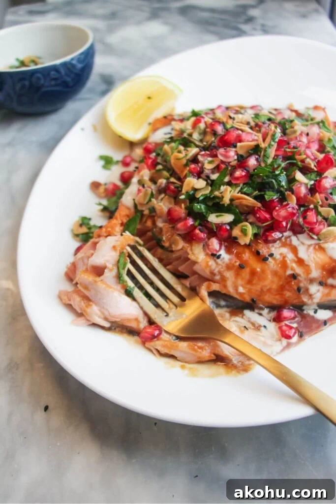 Close up of a fork flaking pieces of salmon from a salmon fillet, topped with pomegranate salsa.