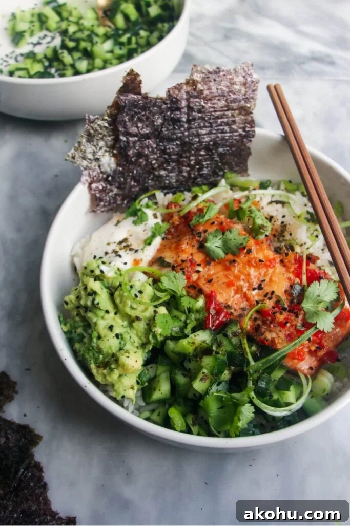 White bowl filled with colourful vegetables and a salmon fillet with seaweed sheets on the side and chopsticks in the bowl.