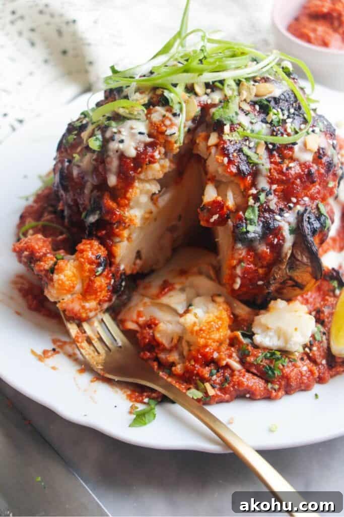 Whole roasted cauliflower with a slice cut out of it, with a fork piercing a piece of cauliflower.