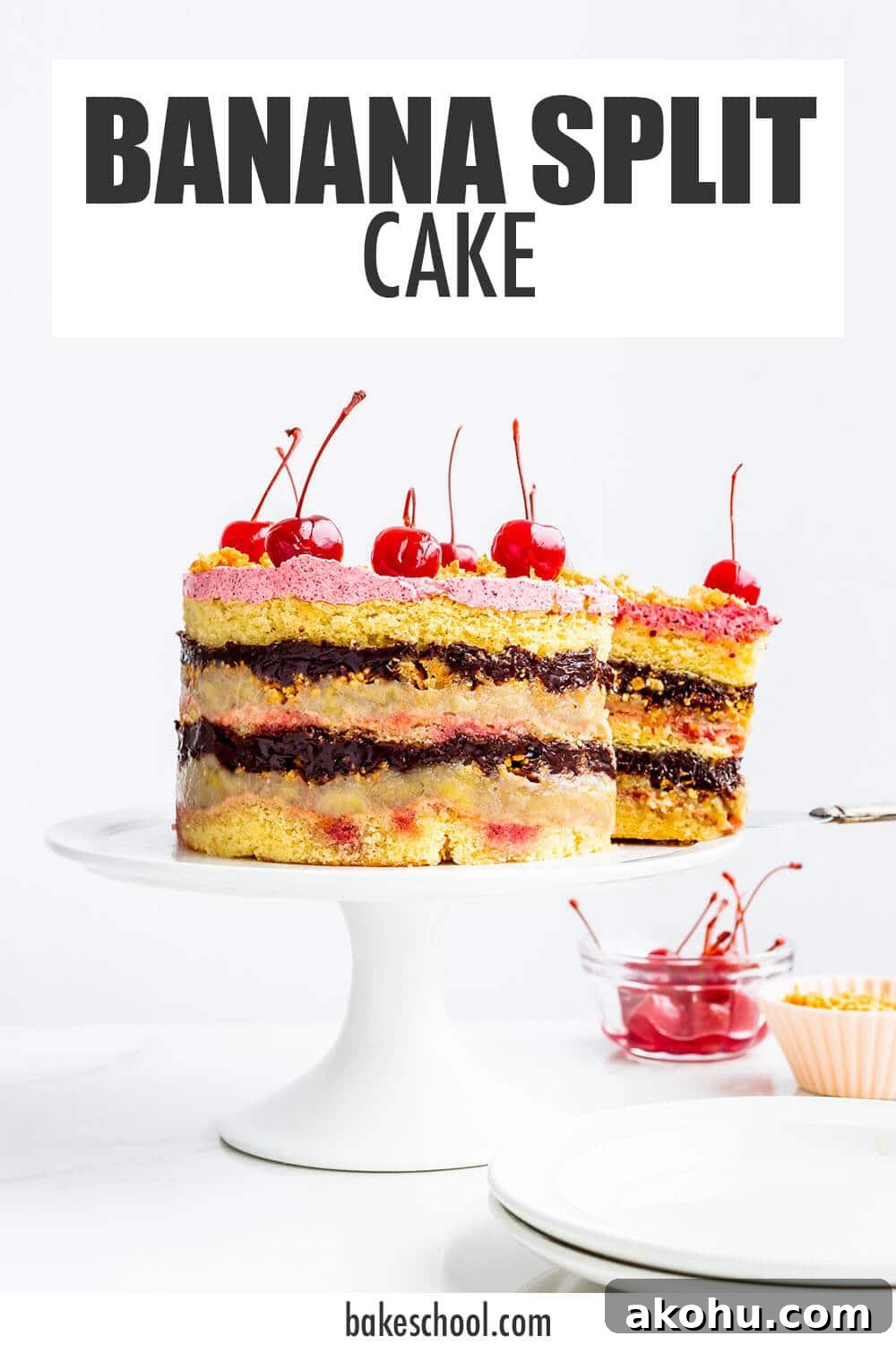 Banana split layer cake topped with maraschino cherries on a cake stand.