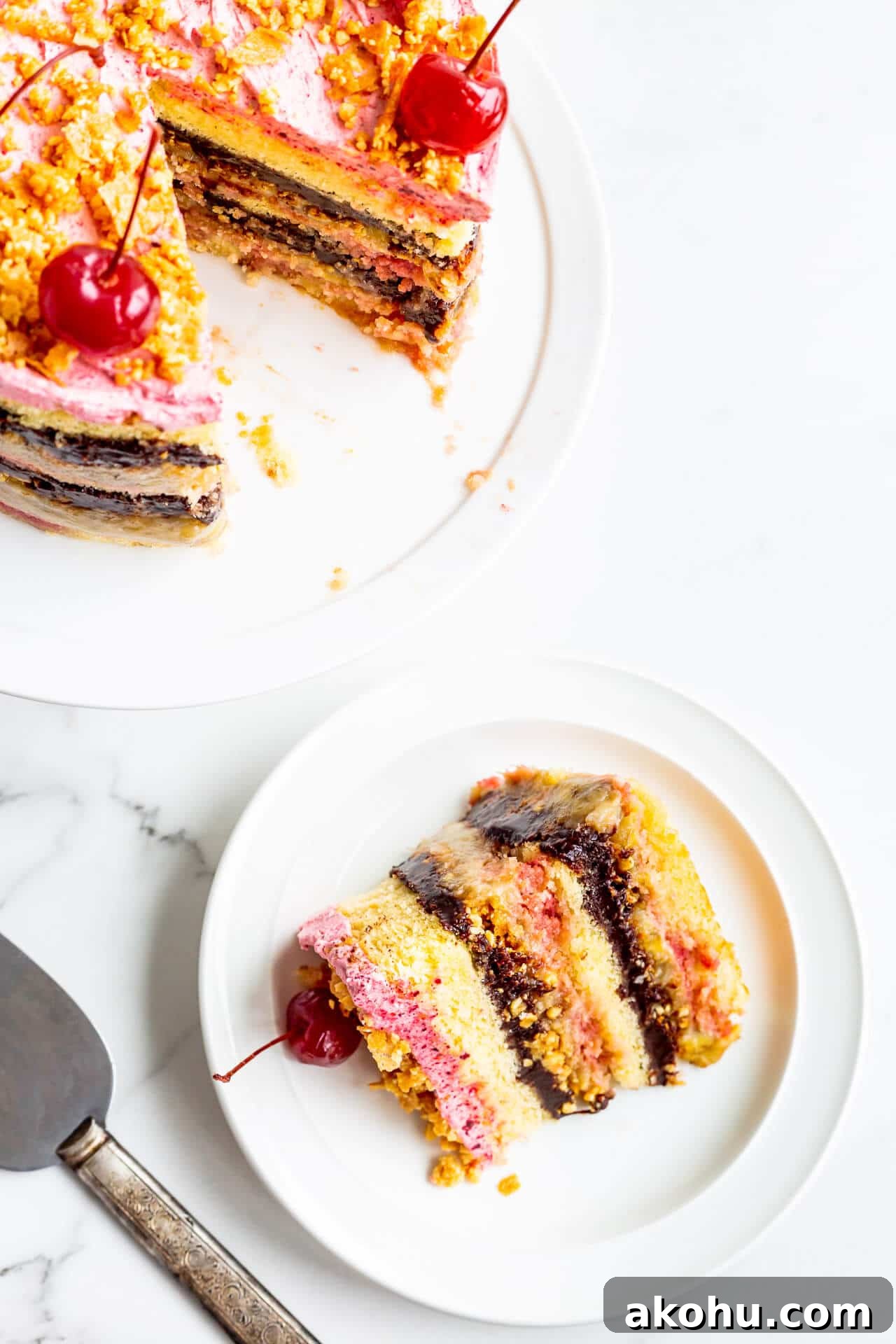 Banana split layer cake topped with maraschino cherries on a cake stand being served on plates.
