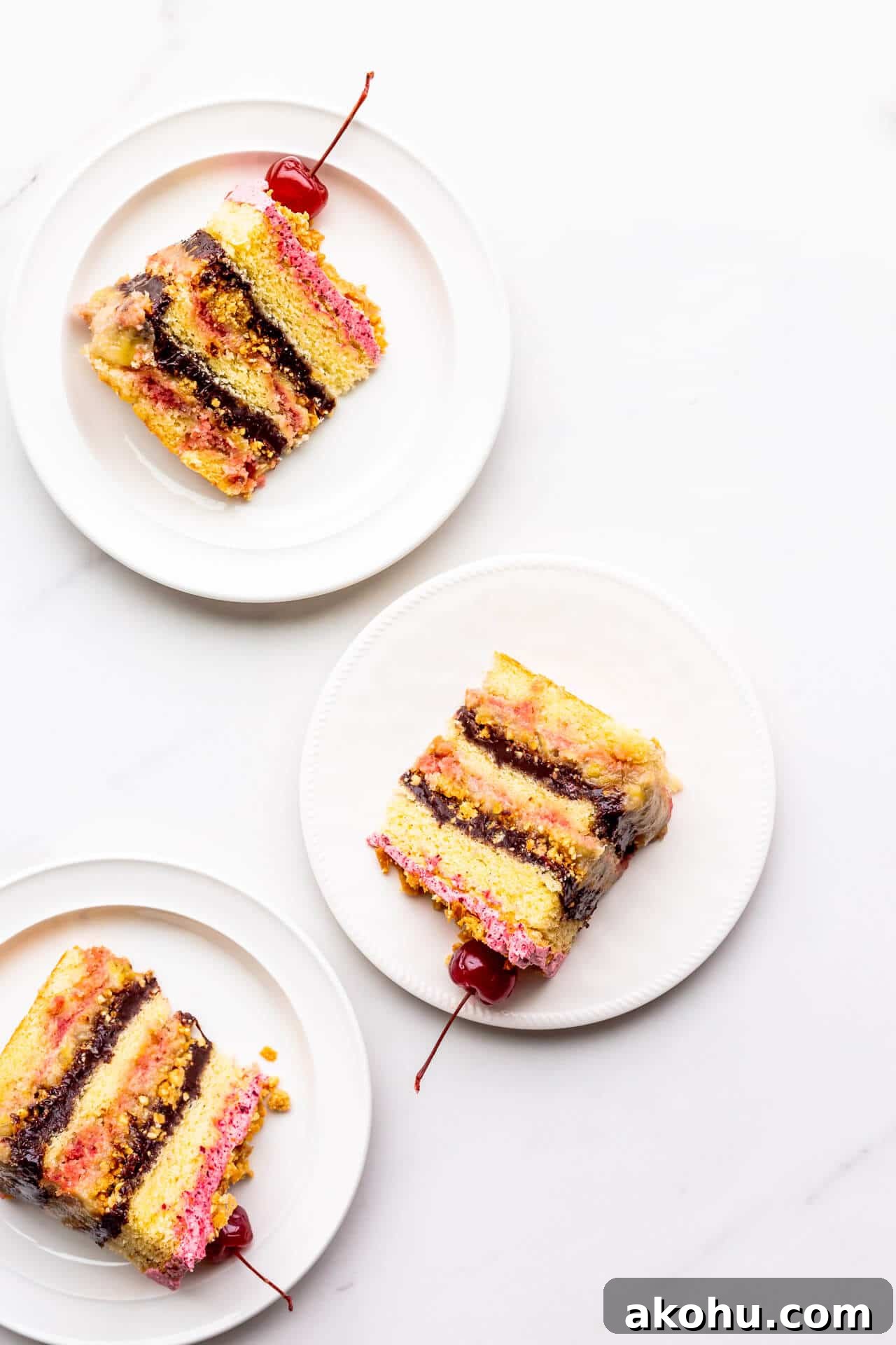 Slices of banana split cake topped with maraschino cherries, served on plates.