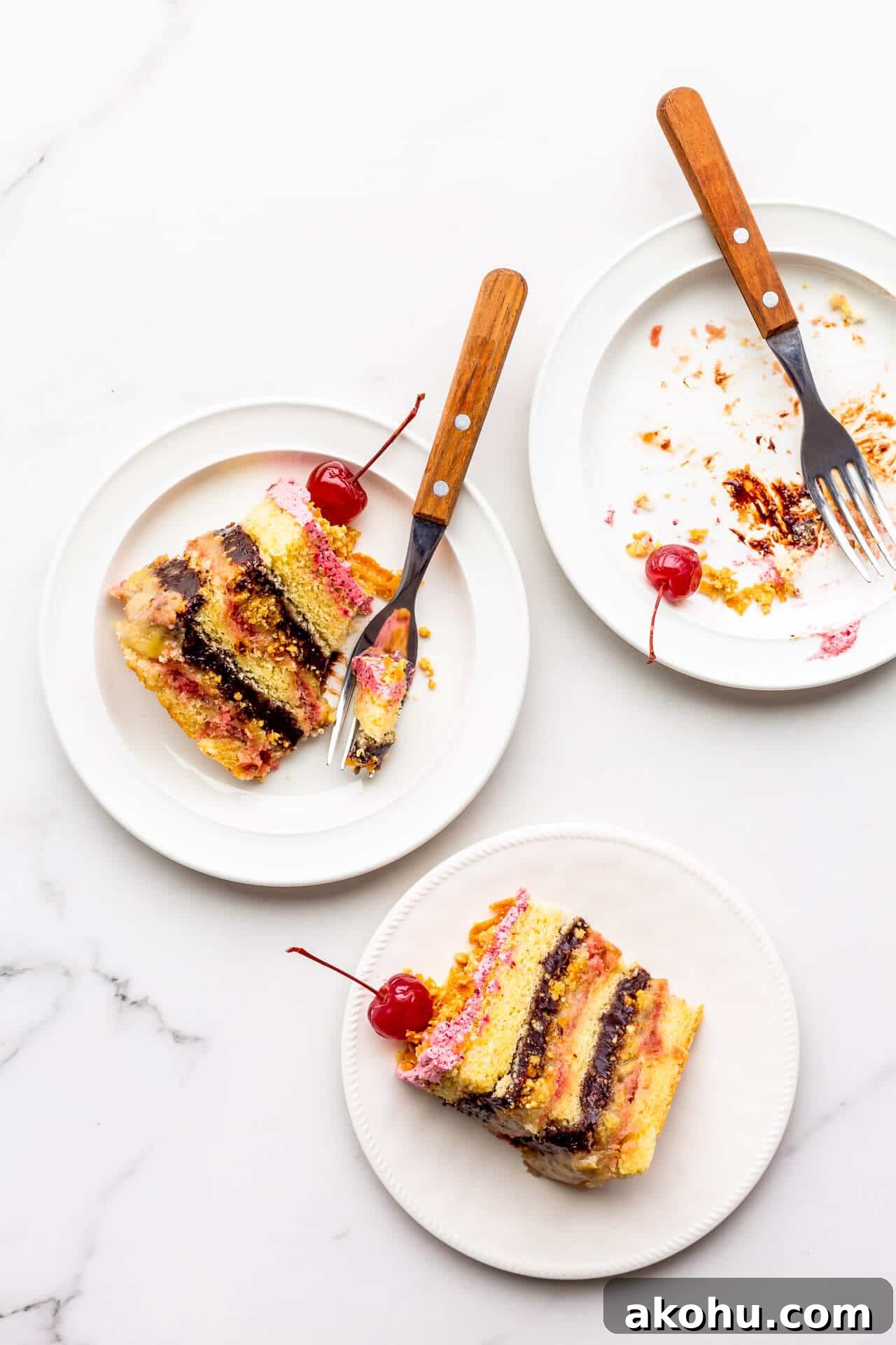 Slices of banana split cake topped with maraschino cherries, served on plates, with one slice eaten.
