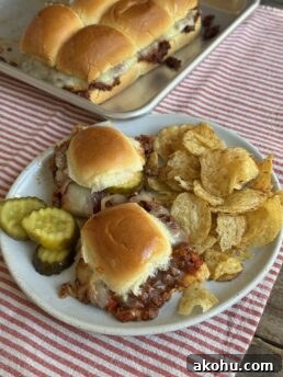 two sloppy joe sliders on a plate with chips and pickles