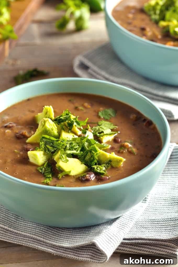 Two green bowls of black bean soup topped with chopped avocado and cilantro.