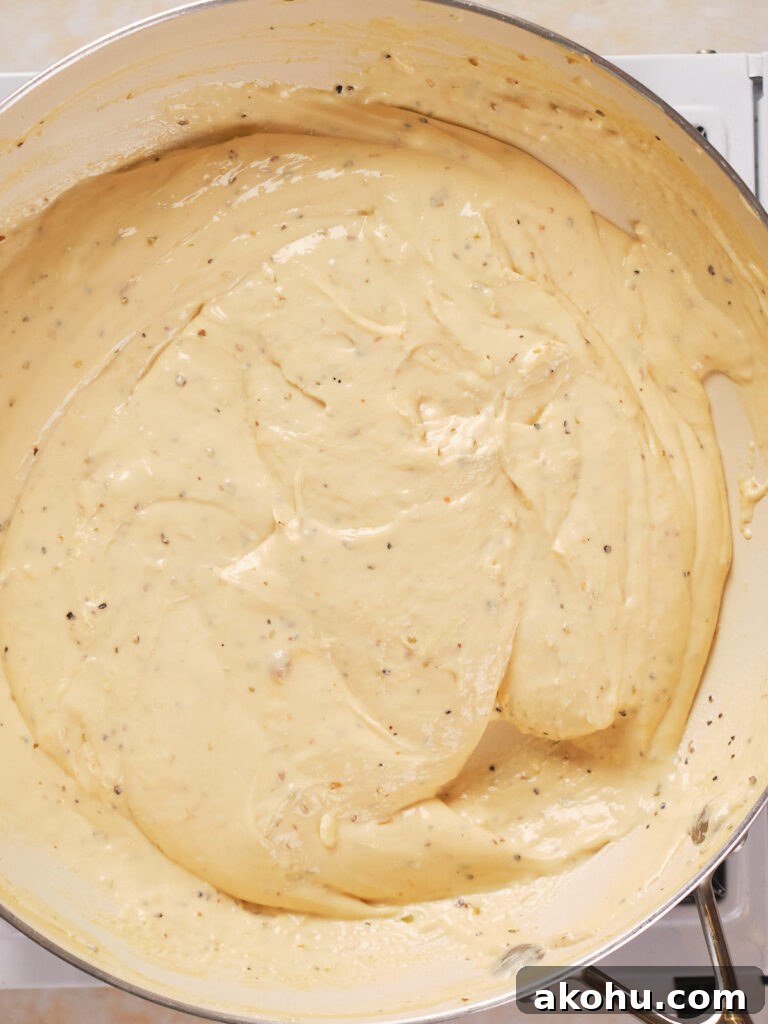 Keto Cauliflower Mac and Cheese: 4-Step Low-Carb Recipe 6 A close-up of creamy sauce with visible herbs cooked in a large pan.