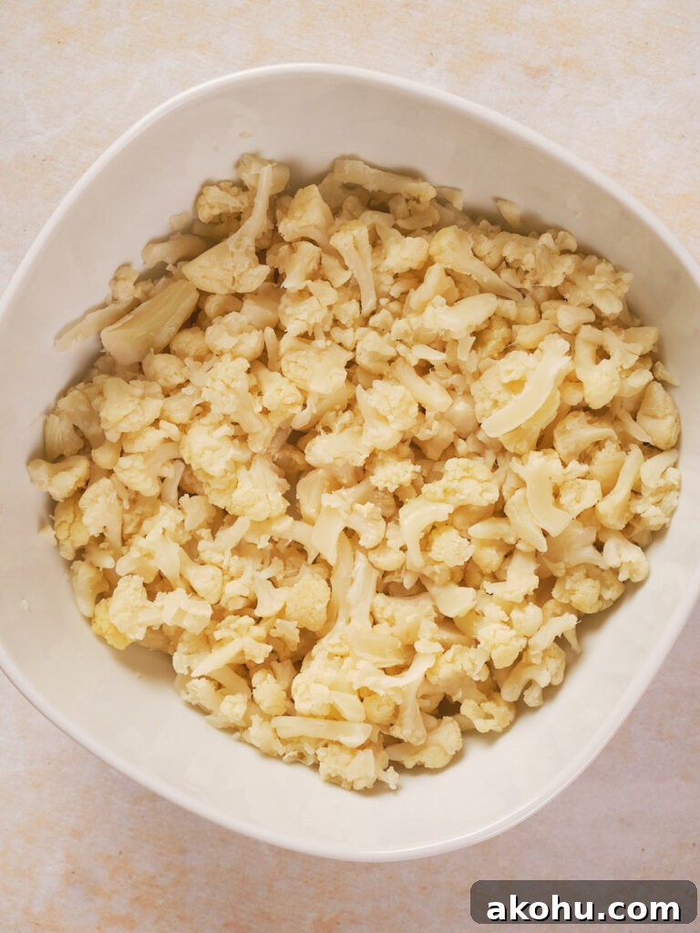 Keto Cauliflower Mac and Cheese: 4-Step Low-Carb Recipe 7 A white bowl filled with chopped cauliflower pieces on a light surface.