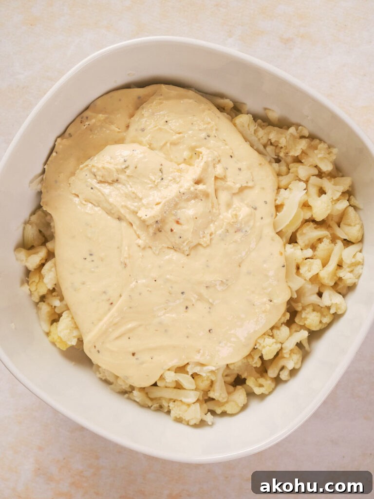 Keto Cauliflower Mac and Cheese: 4-Step Low-Carb Recipe 8 A white bowl filled with chopped cauliflower topped with a thick, creamy sauce.