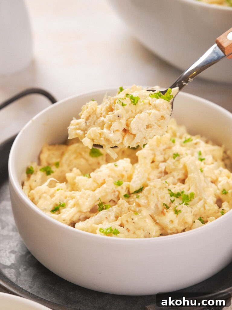 Keto Cauliflower Mac and Cheese: 4-Step Low-Carb Recipe 9 A bowl of creamy casserole garnished with green herbs, with a spoon lifting a portion.