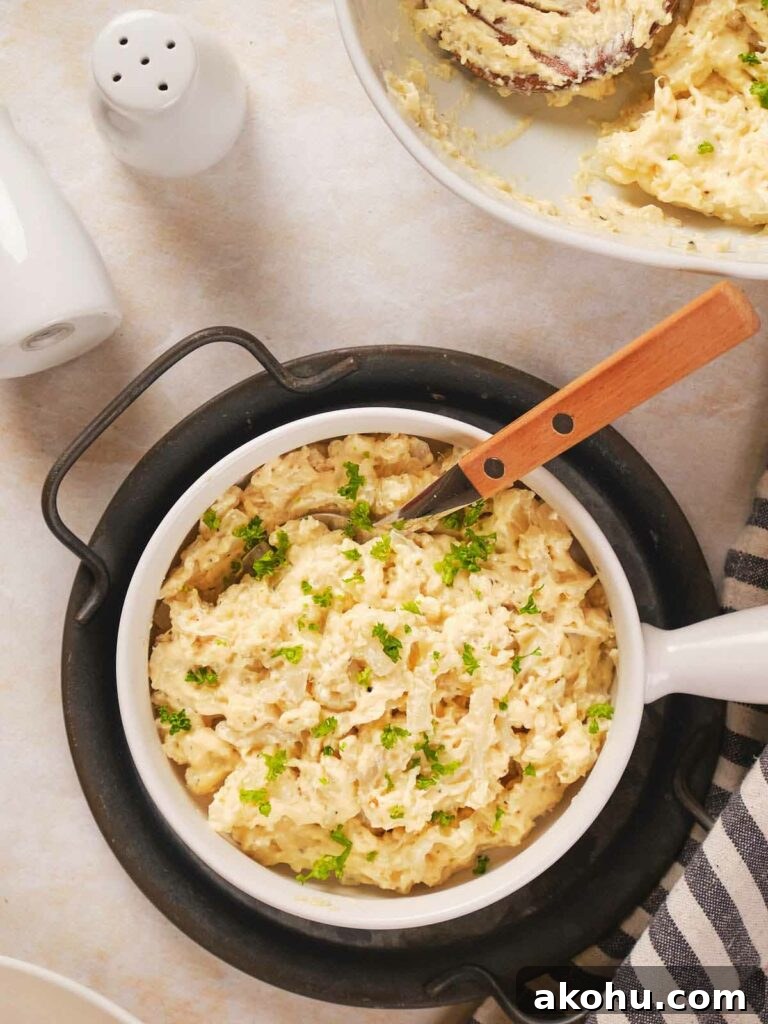 Keto Cauliflower Mac and Cheese: 4-Step Low-Carb Recipe 10 A bowl of mashed potatoes with herbs on top, accompanied by a knife with a wooden handle.