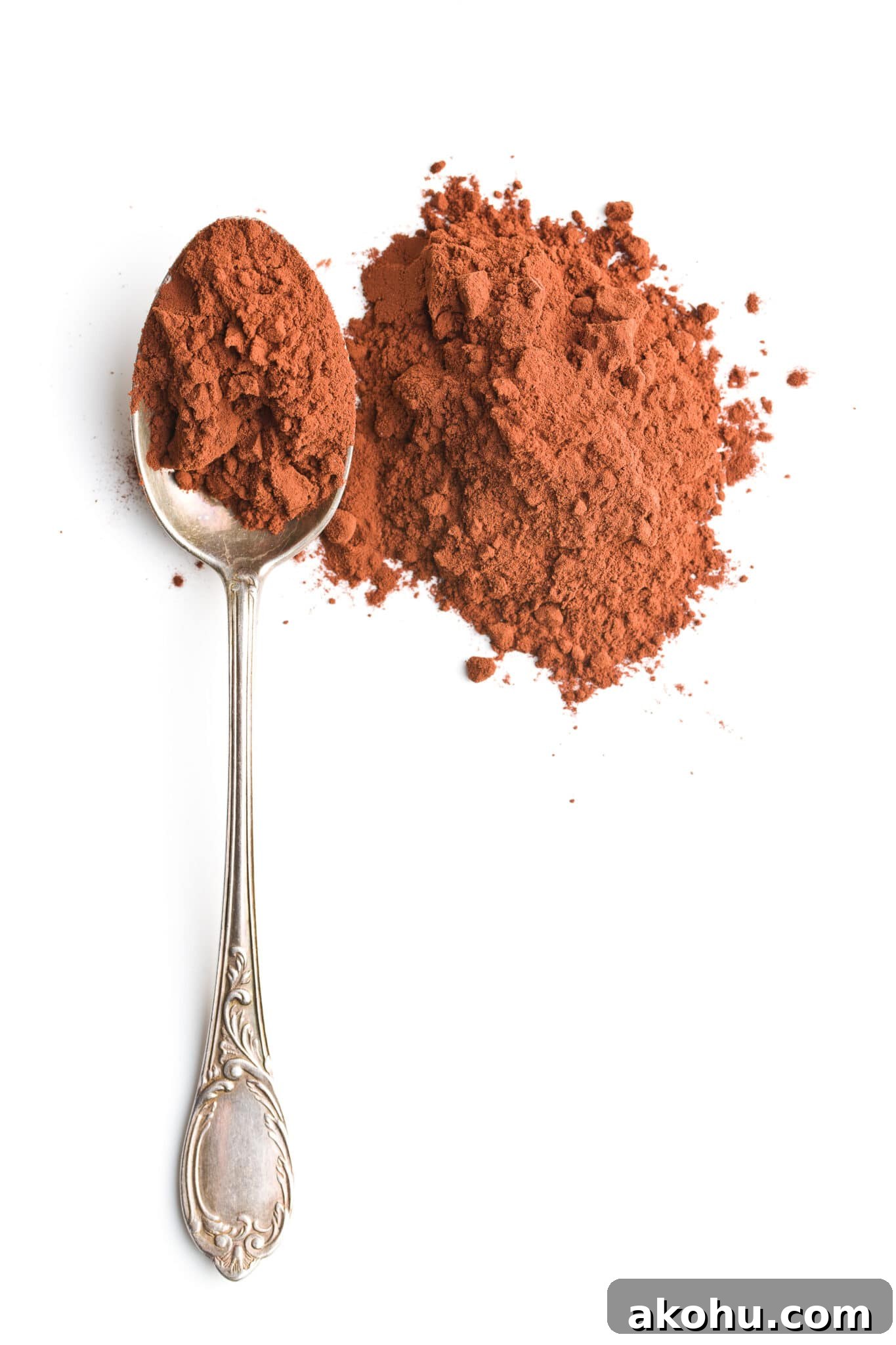A silver tablespoon filled with cocoa powder isolated on a bright white background.