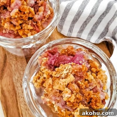 Two dessert cups filled with pineapple cherry dump cake, sitting on a cutting board next to a kitchen towel