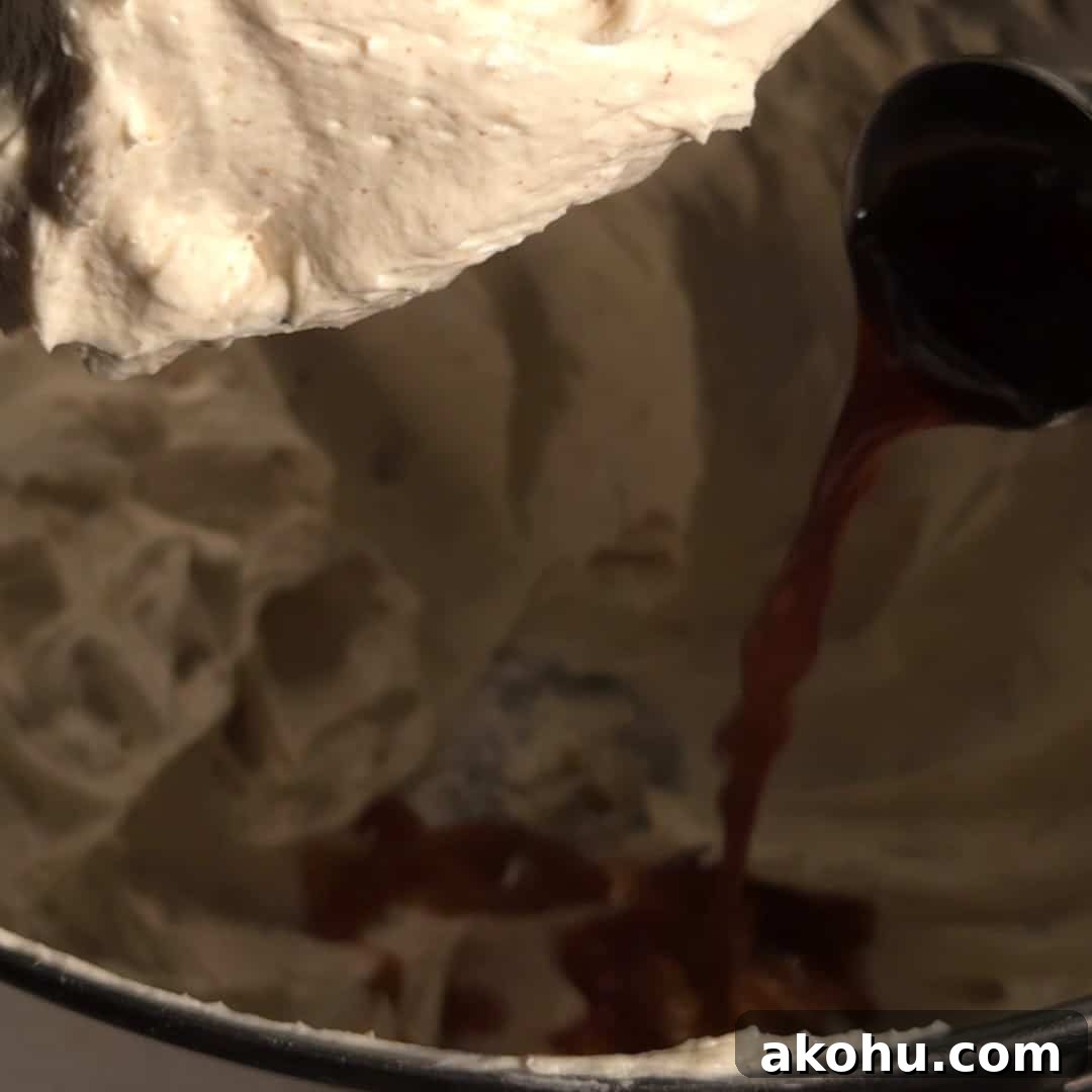 Brown butter being poured into cream cheese mixture in a mixing bowl to make browned butter cream cheese frosting.